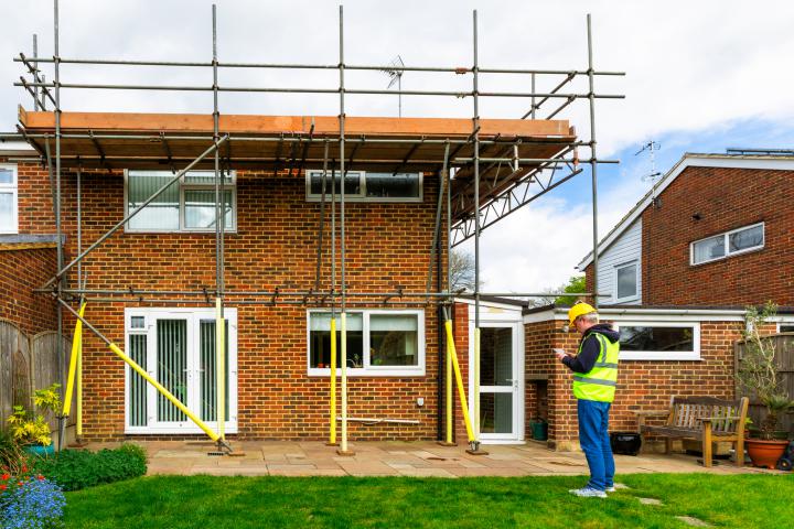 Construction worker examining scaffolding on a semi detached house undergoing renovation